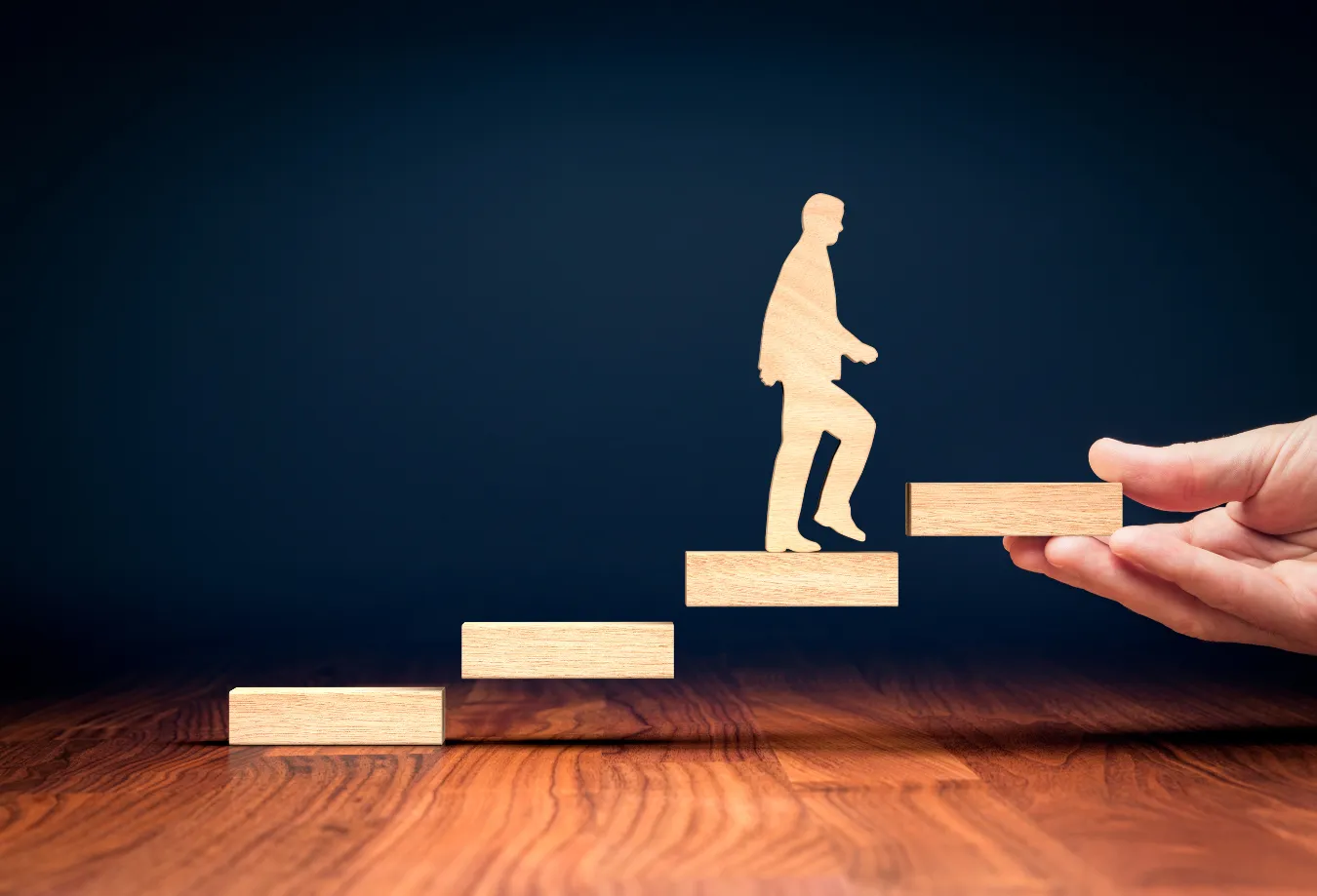 Image: A side-view of a human hand showing a human-like figurine climbing stairs, showing the importance of leadership development in workplace