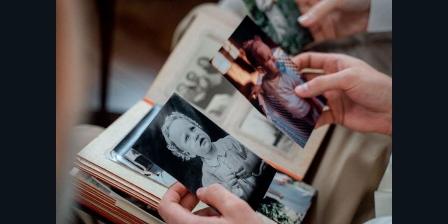 Close-up of hands holding black-and-white and color family photographs pulled from an old photo album, representing how legacy brands transform their history into future growth